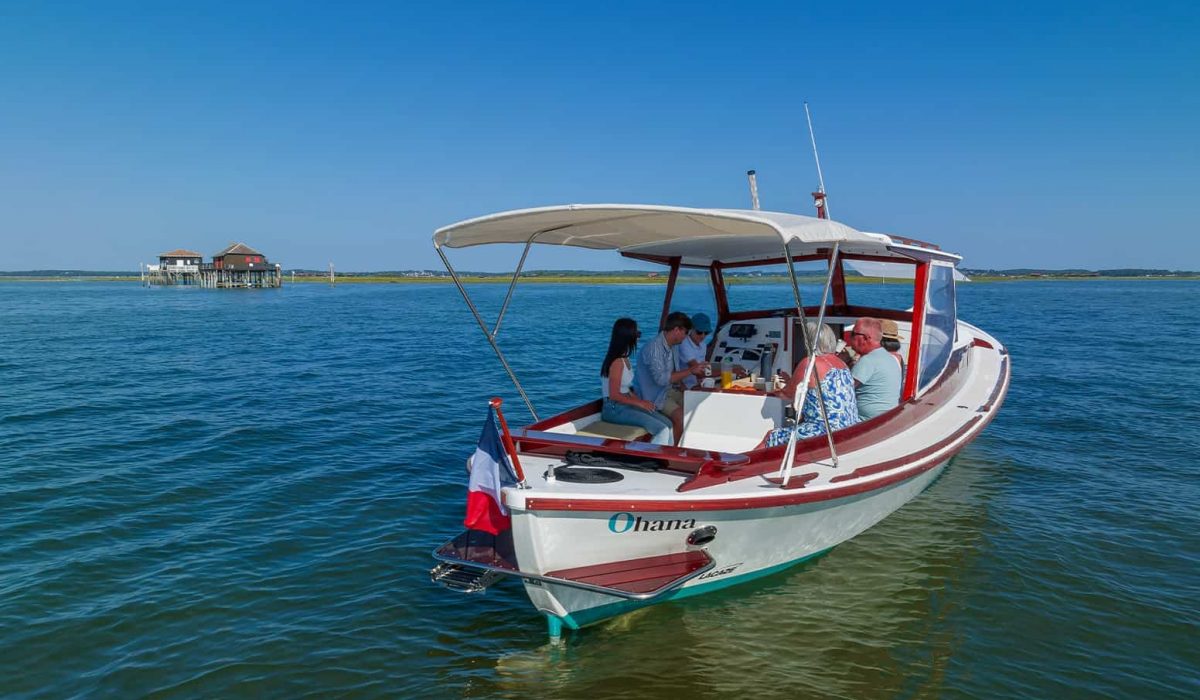 Photo ou l'on voit des personnes profitant d'une balade en pinasse avec en toile de fond les cabanes tchanquees